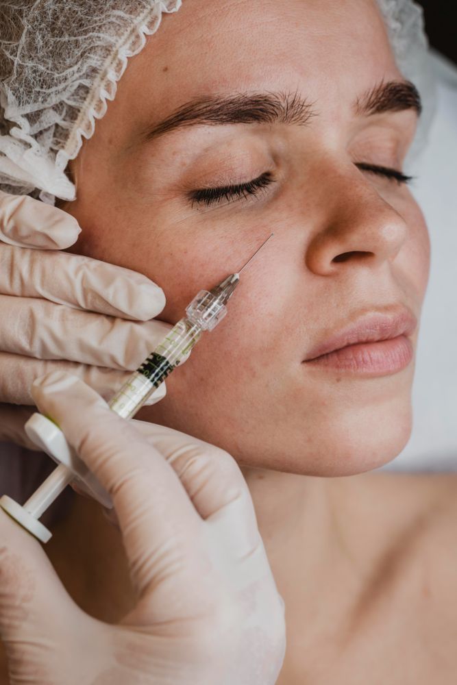 A woman receiving a facial injection in a clinical setting, focused on her face and the medical professional's hands.