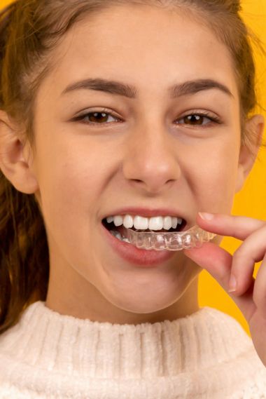 young girl holding clear aligner to her mouth