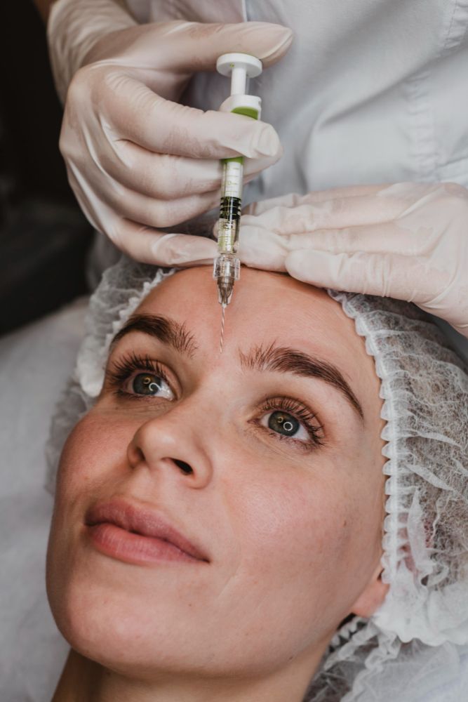 A woman receiving a facial injection in a clinical setting, focused on her face and the medical professional's hands.