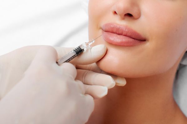Lip shape correction procedure cosmetologist making an injection on lips of young lady patient closeup shot lip augmentation concept